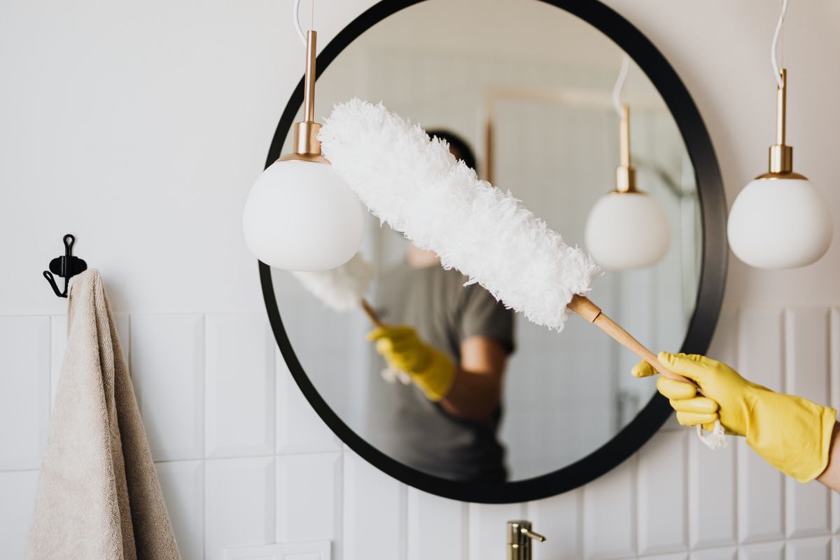 Cleaner dusting a bathroom mirror and pendant lights